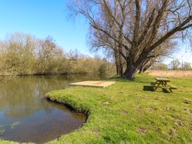 A riverbank with grassy area trees a wooden platform and a picnic table at Wayford Mill in Wayford
