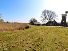 A grassy field with a large tree and a windmill near a brick house and barn at Wayford Mill in Wayford
