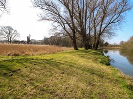 A riverside scene with tall trees and a windmill structure in the background at Wayford Mill in Wayford
