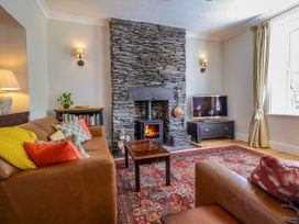 A living room with a stone fireplace a wood stove two leather sofas a small table a television on a stand and a patterned rug at Glan yr Afon in Abergynolwyn near Tywyn