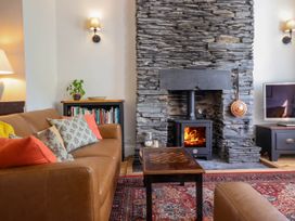 A living room with a leather sofa cushions a wood burning stove in a stone fireplace and a television at Glan yr Afon in Abergynolwyn near Tywyn