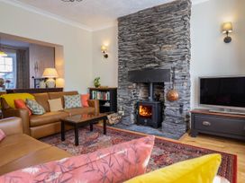 A living room with a stone fireplace a wood-burning stove brown leather sofas a coffee table and a television at Glan yr Afon in Abergynolwyn near Tywyn