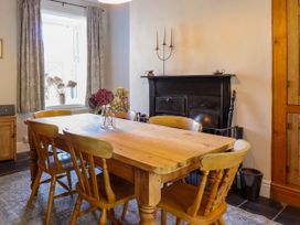 A dining room with a wooden table and chairs a black fireplace and a window with curtains at Glan yr Afon in Abergynolwyn near Tywyn