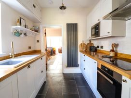 A kitchen with white cabinets wooden countertops a sink a stove a microwave and a black radiator at Glan yr Afon in Abergynolwyn near Tywyn