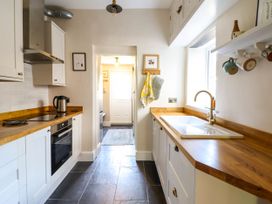 A kitchen with white cabinets wooden countertops a black stove a kettle a white sink and mugs hanging near a window at Glan yr Afon in Abergynolwyn near Tywyn