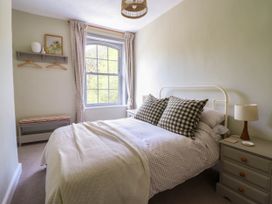 A bedroom with a bed with checkered pillows and a blanket near a window with curtains and a bedside table with a lamp at Glan yr Afon in Abergynolwyn near Tywyn