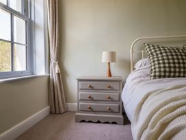A bedroom with a window and curtain next to a bedside table with a lamp and a bed with checked pillows at Glan yr Afon in Abergynolwyn near Tywyn