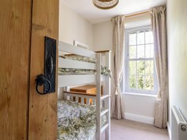A small bedroom with white bunk beds a wooden chest of drawers and a window with curtains at Glan yr Afon in Abergynolwyn near Tywyn
