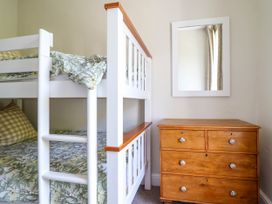 A bunk bed with floral bedding next to a wooden chest of drawers and a wall mirror at Glan yr Afon in Abergynolwyn near Tywyn
