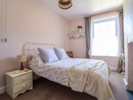 A bedroom with a double bed near a window a bedside table with a lamp and a wall shelf with hangers at Glan yr Afon in Abergynolwyn near Tywyn