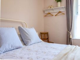 A bedroom with a bed with pillows and floral bedding a wooden chair a shelf with hangers and a window with curtains at Glan yr Afon in Abergynolwyn near Tywyn