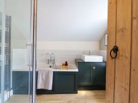 A bathroom with a bathtub, a towel hanging, a sink on a cabinet, and a wooden door at Glan yr Afon in Abergynolwyn near Tywyn