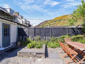 A small fenced garden with a raised flower bed and wooden table and chairs at Glan yr Afon in Abergynolwyn near Tywyn