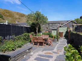 An outdoor patio area with a wooden dining table and chairs surrounded by plants and stone walls at Glan yr Afon in Abergynolwyn near Tywyn