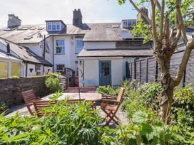 An outdoor patio with wooden table and chairs surrounded by plants and a two story house at Glan yr Afon in Abergynolwyn near Tywyn
