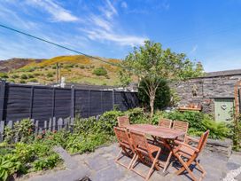 An outdoor patio with a wooden table and six chairs surrounded by plants and a tree at Glan yr Afon in Abergynolwyn near Tywyn