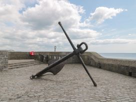 A large anchor on a paved area near a stone wall with the sea and sky in the background at Teal House in Lyme Regis