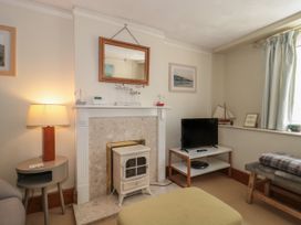 A living room with a fireplace TV on a stand lamp and a bench at Lavender Cottage Lyme Regis
