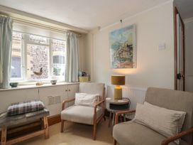 A sitting room with two armchairs a small table with a lamp a bench and a window with curtains at Lavender Cottage in Lyme Regis