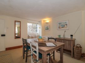 A dining room with a wooden table and mixed chairs next to a window and cabinet at Lavender Cottage in Lyme Regis