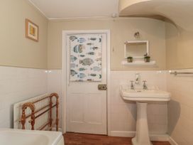 A bathroom with a white pedestal sink a mirror with two small plants a wooden towel rack and a door with a fish patterned curtain at Lavender Cottage in Lyme Regis