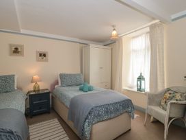 A bedroom with two single beds a nightstand with a lamp a wardrobe a window with curtains and a chair at Lavender Cottage in Lyme Regis