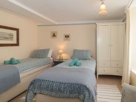 A bedroom with two single beds a nightstand with a lamp a white wardrobe and framed pictures at Lavender Cottage Lyme Regis