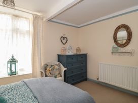 A bedroom with a blue chest of drawers a white wicker chair with a floral cushion a bed with blue and grey bedding and a window with curtains and a decorative lantern at Lavender Cottage Lyme Regis