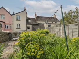 A garden with yellow flowers and green plants next to a stone wall and wooden fence with houses in the background at Lavender Cottage in Lyme Regis