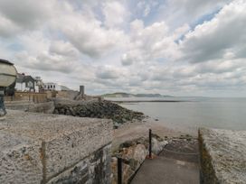 A coastal scene with stone walls and steps leading to a rocky shoreline and calm sea with buildings in the background at Lavender Cottage in Lyme Regis