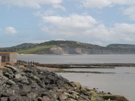 A rocky shoreline with a stone wall and railings overlooking water and a distant cliff with greenery at Lavender Cottage in Lyme Regis
