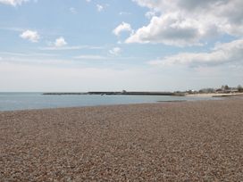 A pebble beach with calm sea and sky with clouds and buildings in the distance at Lavender Cottage Lyme Regis