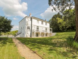 A white two-story house with a balcony and garden path surrounded by trees at The Garden Flat in Charmouth