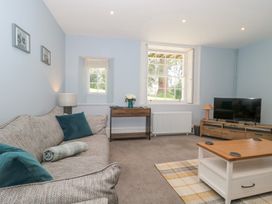 A living room with a sofa, coffee table, television, table lamp, and windows at The Garden Flat in Charmouth