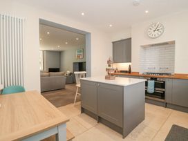 A kitchen with grey cabinets white countertops a wooden dining table and a living room visible through an open doorway at The Garden Flat in Charmouth