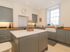 A kitchen with gray cabinets a kitchen island a large window and a wall clock at The Garden Flat in Charmouth