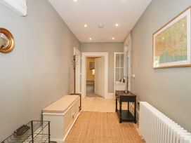 A hallway with a beige bench, a black table with a lamp, a coat rack, a radiator, and a framed map at The Garden Flat in Charmouth