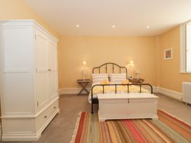 A bedroom with a black metal bed white wardrobe white storage chest bedside tables and a striped rug at The Garden Flat in Charmouth