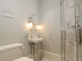 A bathroom with a toilet a sink with round mirror and two lights and a glass door shower at The Garden Flat in Charmouth