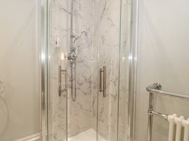 A shower with glass doors and marble tiles in a bathroom at The Garden Flat in Charmouth
