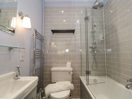 A bathroom with a bathtub shower combination a toilet and a sink with a mirror at The Garden Flat in Charmouth