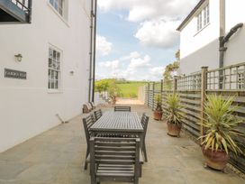 An outdoor patio with a wooden table and six chairs and potted plants along a wooden fence at The Garden Flat in Charmouth