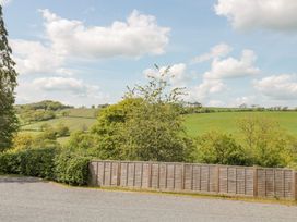 A fenced garden with trees and green fields under a cloudy sky at The Garden Flat in Charmouth
