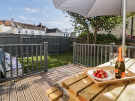 A garden with a wooden deck table holding a tray with strawberries a bottle and glasses next to a closed grey fence and houses at 5 Stafford Road in Paignton