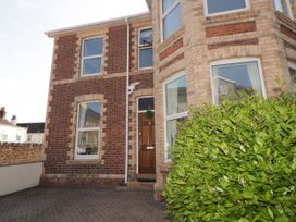 The front entrance of a brick house with a wooden door a plant bush to the right and windows above and beside the door at 5 Stafford Road Paignton