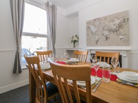 A dining room with a wooden table set with plates glasses and cutlery six wooden chairs a window with curtains a world map on the wall and a vase with flowers at 5 Stafford Road Paignton