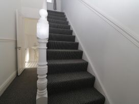 A staircase with carpet and a white newel post next to an open door showing a small room with a sink at 5 Stafford Road in Paignton