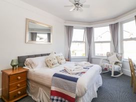 A bedroom with a bed side table a bed with pillows and folded towels a rocking chair and windows with curtains at 5 Stafford Road in Paignton