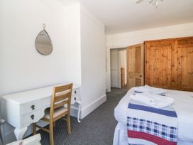 A bedroom with a bed covered in a blue white and red blanket a wooden wardrobe a white desk with a wooden chair and a mirror on the wall at 5 Stafford Road in Paignton