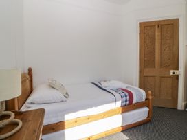 A single bed with a wooden frame and white bedding next to a wooden door and a small wooden bedside table with a lamp at 5 Stafford Road in Paignton
